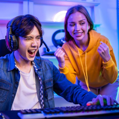 Caucasian Esport couple gamer playing online video game on computer. Handsome man gaming player feel happy and excited, enjoy technology broadcast live streaming while plays cyber tournament at home